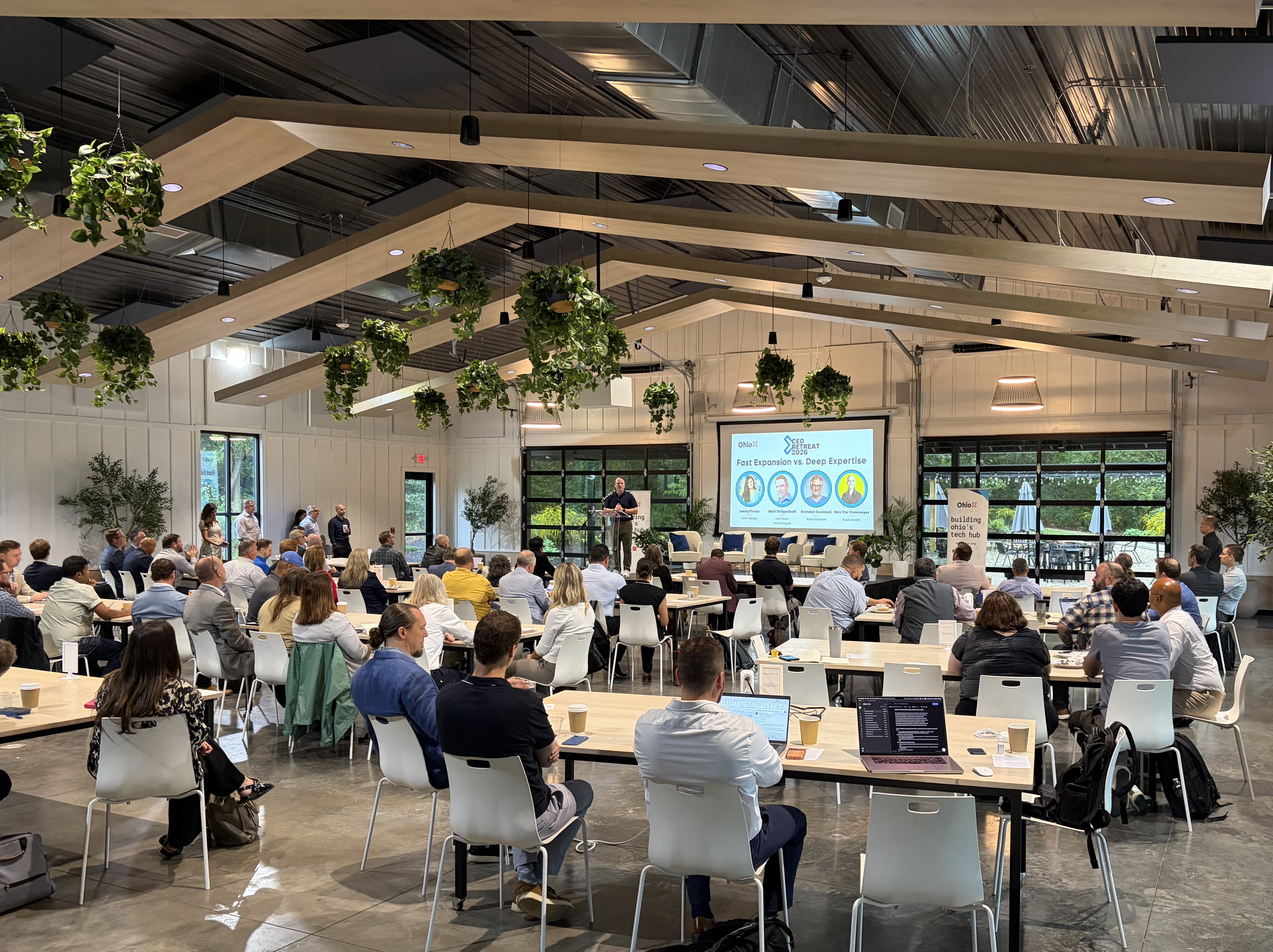 The OhioX CEO Retreat gathering at Retreat 21, with attendees seated at tables beneath timber beams and hanging plants